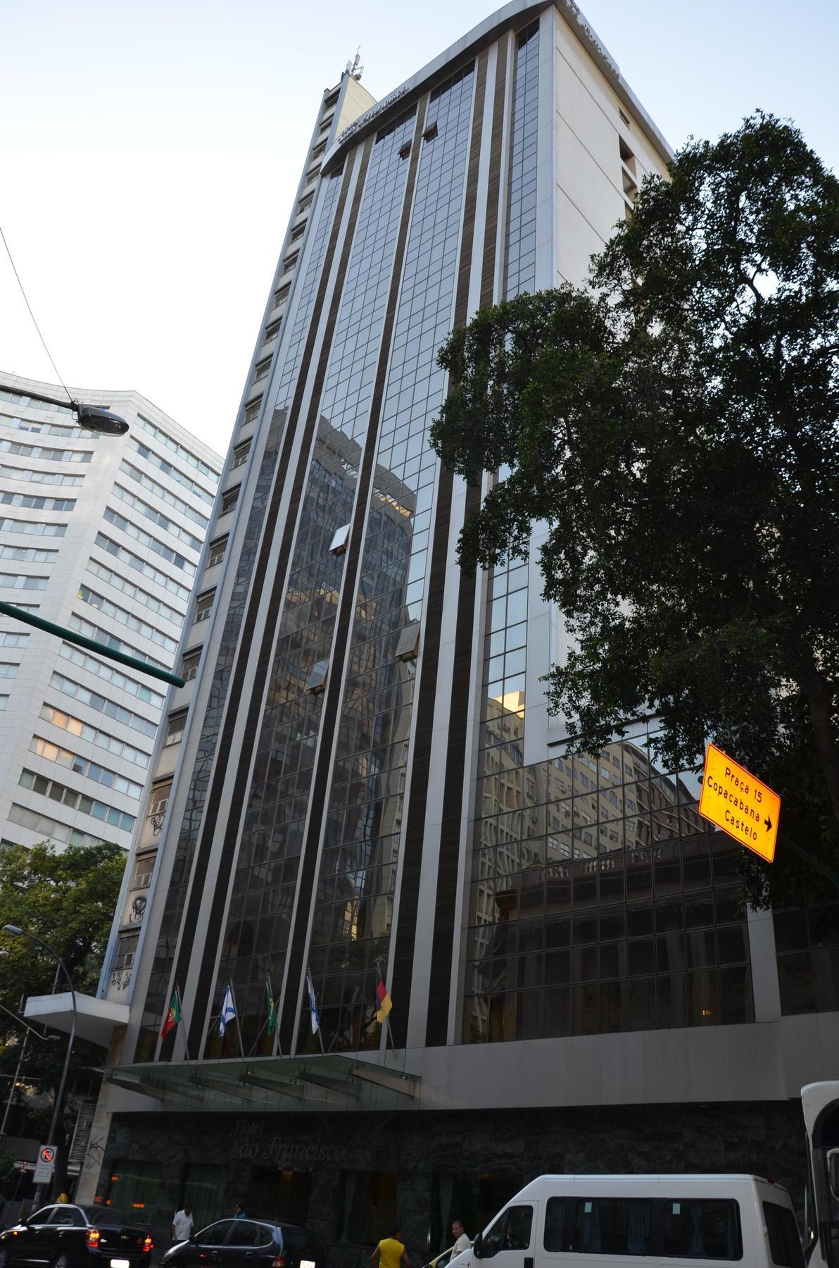 Hotel Atlantico Tower ริโอเดจาเนโร ภายนอก รูปภาพ The photo shows a city street with tall buildings. In the foreground, there is a modern glass skyscraper featuring reflective surfaces and vertical lines. Next to it, there's another building with a different architectural style, also made of glass. 